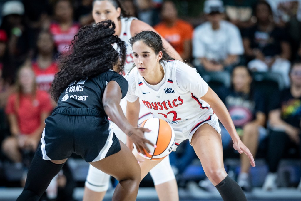 Washington Mystics guard Sonia Citron crouches in a defensive stance with her hands near her knees. Her eyes are laser focused on the player she's defending, Las Vegas Aces guard Dana Evans, who is directly in front of her.