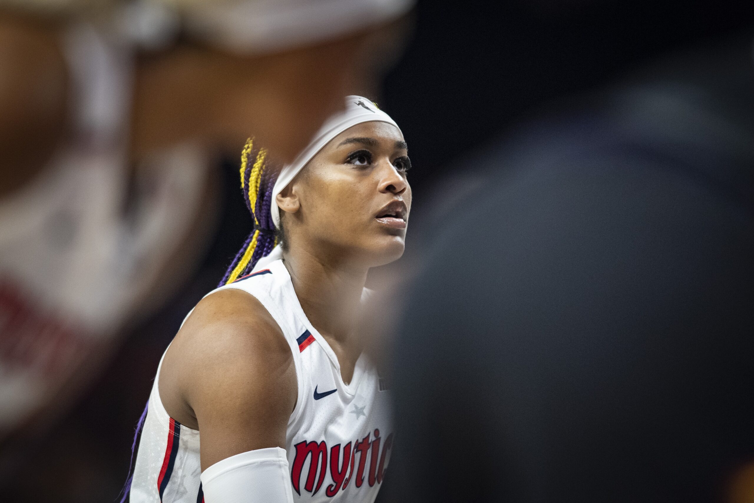 Washington Mystics forward Aaliyah Edwards is shown in profile from the chest up, wearing a white headband and a white Mystics jersey. She is looking up and straight ahead of her.
