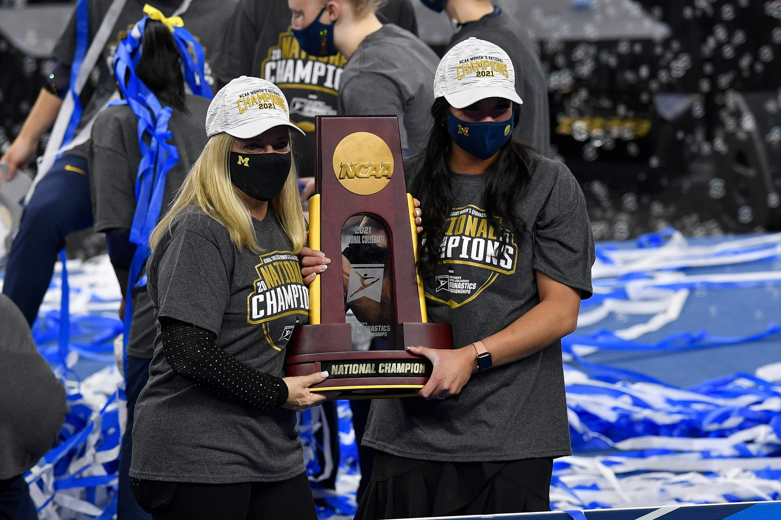 Two women, including Michigan head coach Bev Plocki, in masks accept a trophy.