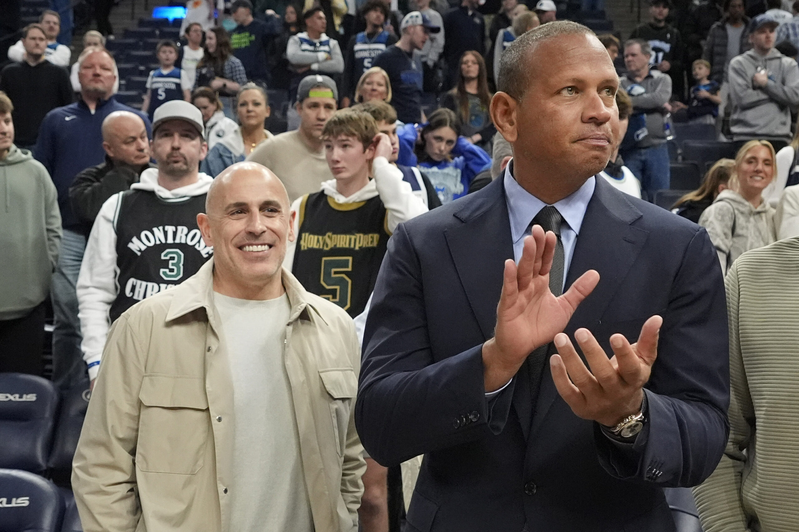 Alex Rodriguez wearing a suit claps his hands at a Timberwolves game in the foreground, Marc Lore is dressed in beige in the background