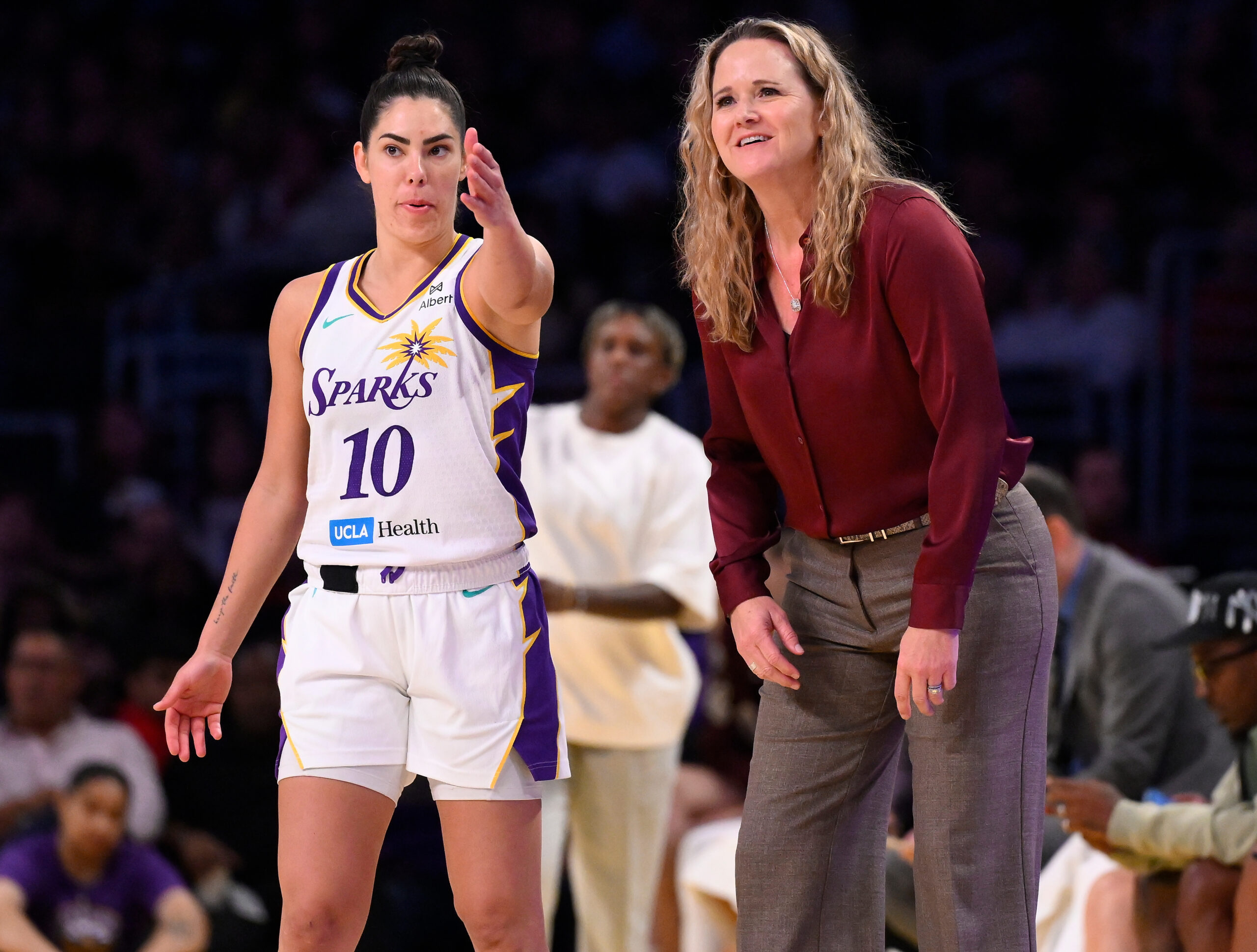 Los Angeles Sparks Coach Lynne Roberts confers with Sparks guard Kelsey Plum, who points to something on the court as Coach Roberts smiles.