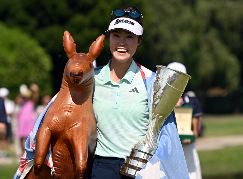 Grace Kim, from Australia, holds the Amundi Evian trophy in her left hand and an inflatable kangaroo under her right arm. The Australian flag is draped around her shoulders and she has a big smile on her face.
