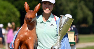 Grace Kim, from Australia, holds the Amundi Evian trophy in her left hand and an inflatable kangaroo under her right arm. The Australian flag is draped around her shoulders and she has a big smile on her face.