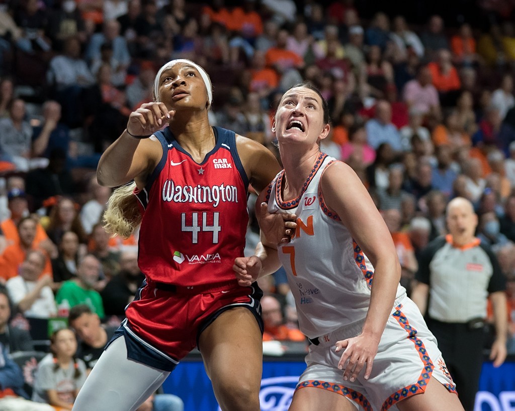 Washington Mystics forward Kiki Iriafen and Connecticut Sun forward Haley Peters push on each other with their forearms as they battle for rebounding position. Both are facing the camera but have their eyes focused upward, on the ball that's out of the frame.