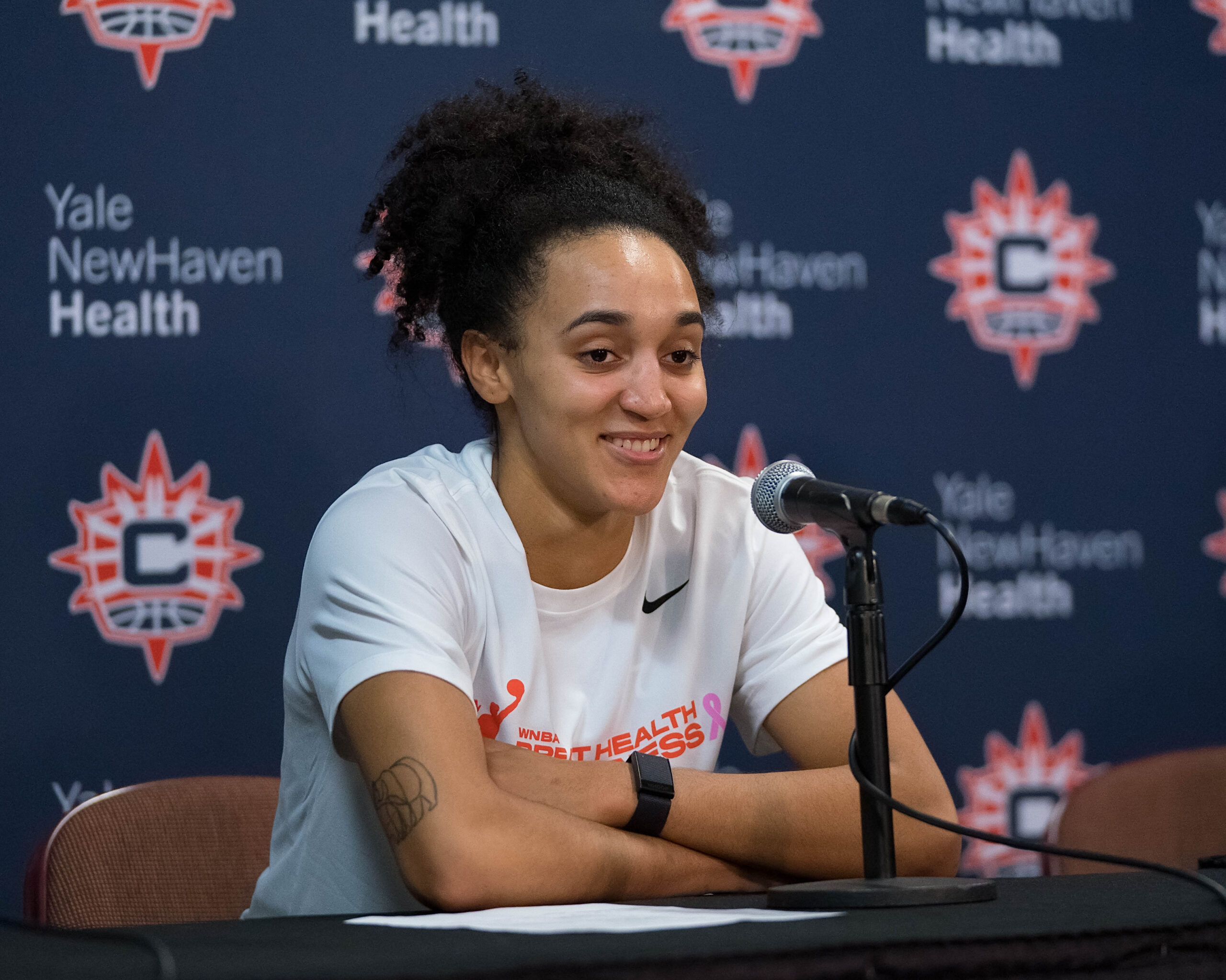 Leïla Lacan smiling with her arms crossed resting on a black clothed table.