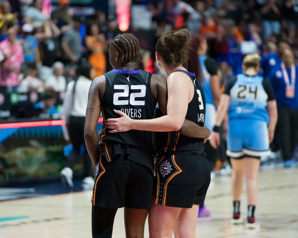 Two players in black uniforms put their arms around each other in support during a game.