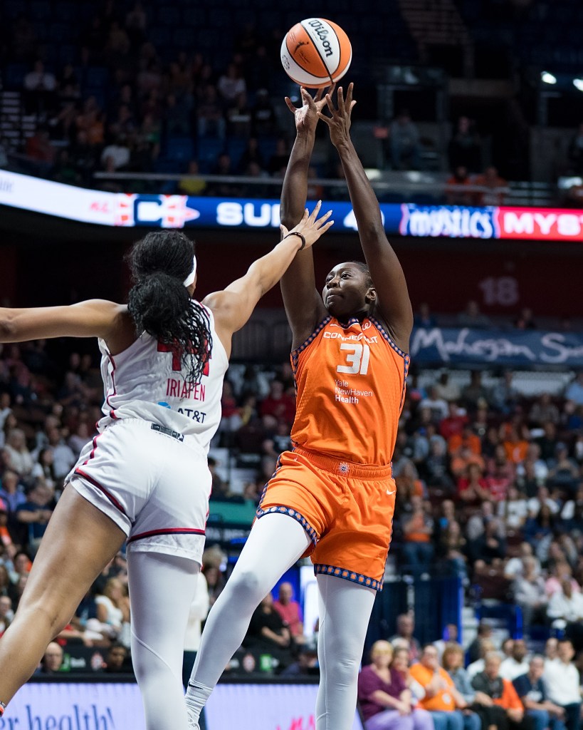 Connecticut Sun center Tina Charles shoots a one-legged fadeaway jump shot. Washington Mystics forward Kiki Iriafen reaches her right hand out to try to contest it.