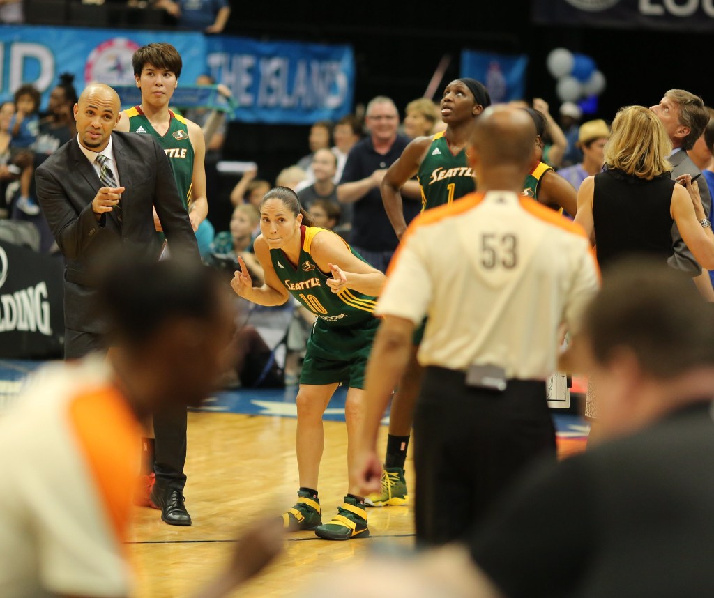 Sue Bird in the middle of a crowd of Seattle Storm players on the court in a game in 2015. She is giving a smirk to the refs. 