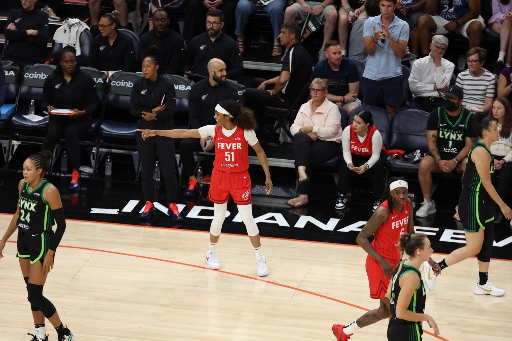 Indiana Fever guard Sydney Colson stands on the 3-point line and points to a teammate who's out of view.