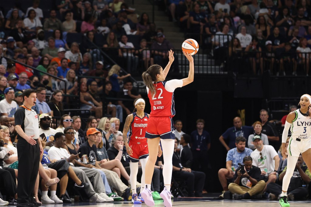 Washington Mystics guard Sonia Citron jumps in the air to take a 3-pointer. The ball is on the fingertips of her right hand, and no defender is near her to contest the shot. She is shown from behind, and the No. 22 on her red jersey is clearly visible at the center of the photo.