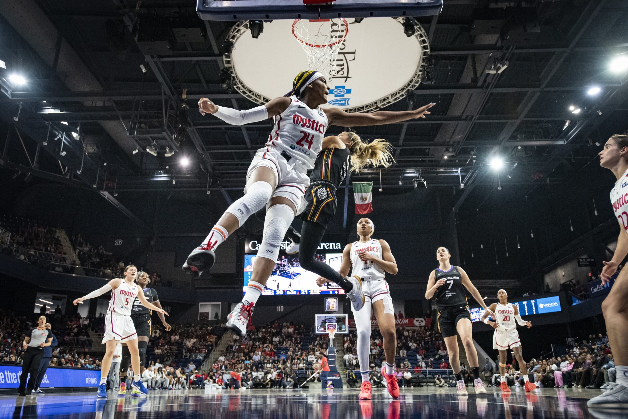 Washington Mystics forward Aaliyah Edwards extends her left arm in midair to try to block an acrobatic layup by Connecticut Sun guard Jacy Sheldon. Sheldon, also in midair, tries to shield the ball from Edwards with her body.