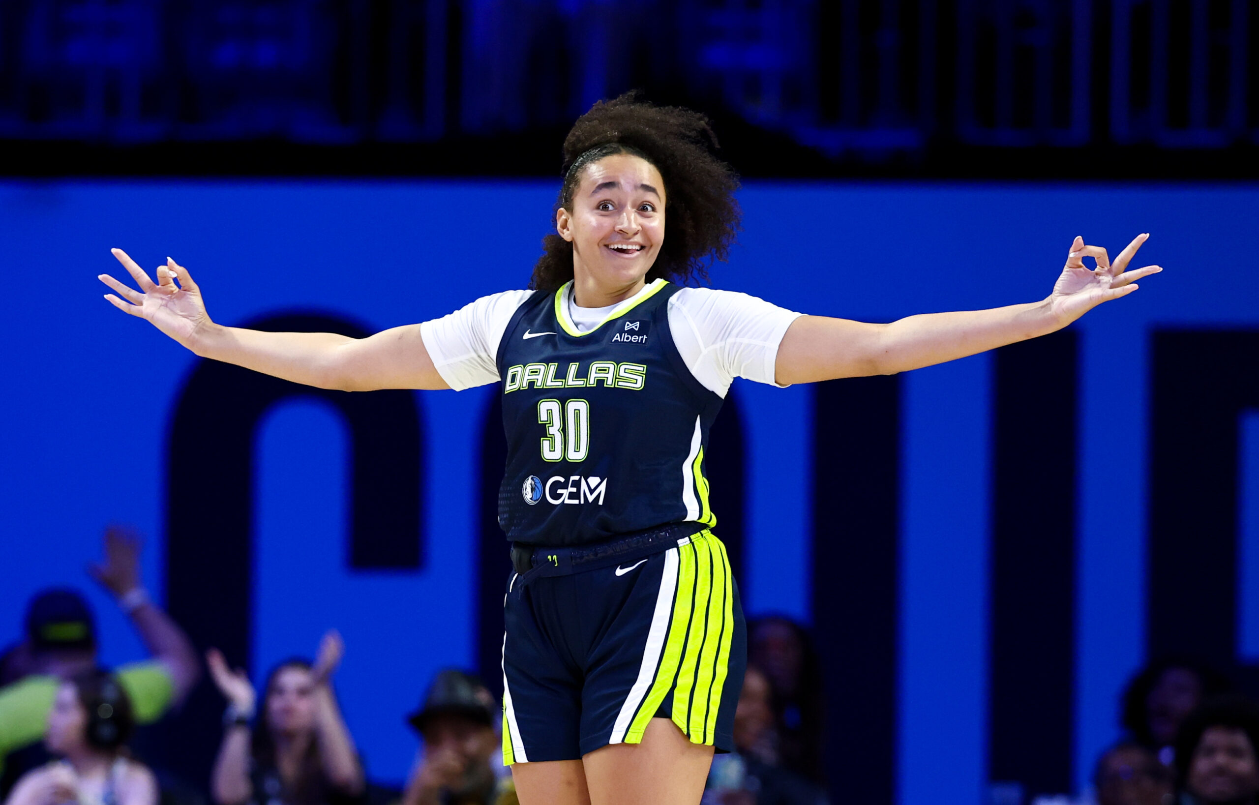 Dallas Wings forward Haley Jones smiles while holding both arms out to the side and making the 3-point sign with each hand.