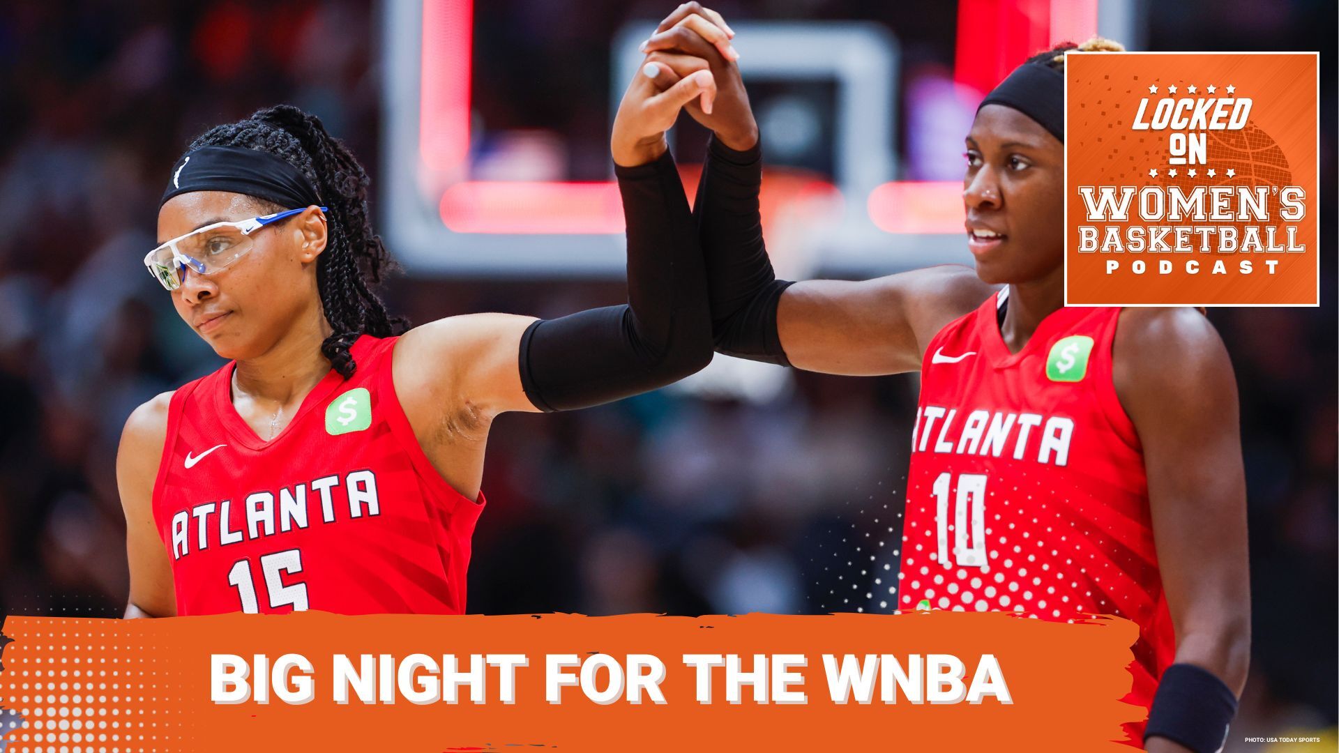 Two players for the Atlanta Dream wearing red jerseys hold hands during a game on the court