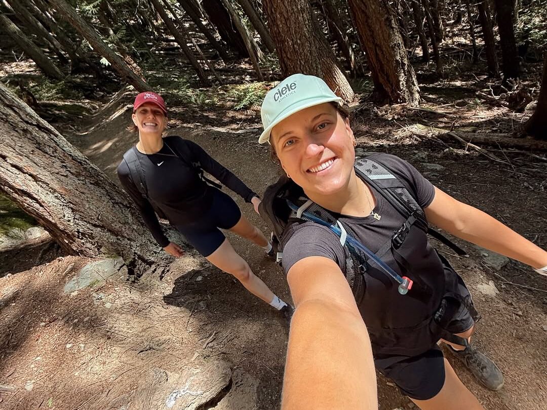 Two women take a hike together and take a selfie. They are both wearing black hiking outfits and smiling.