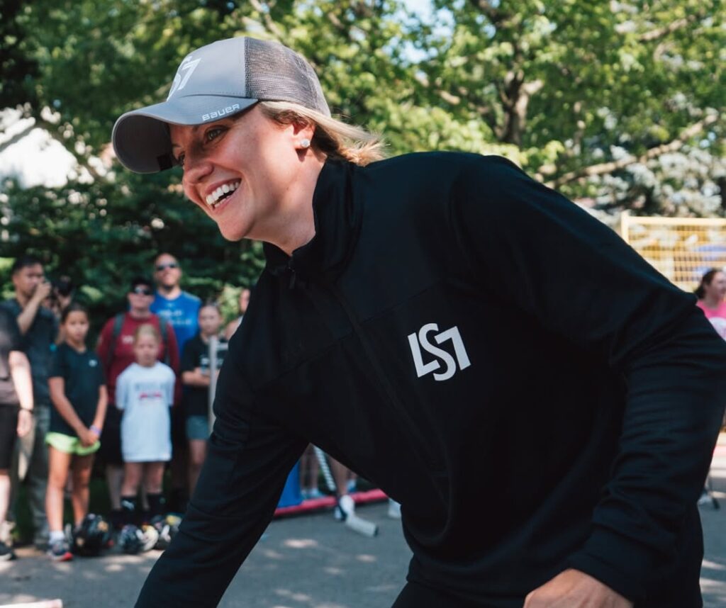 Laura Stacey at her sixth annual LS7 Charity Road Hockey Tournament. She is smiling while wearing a hat and a black quarter-zip that reads LS7.