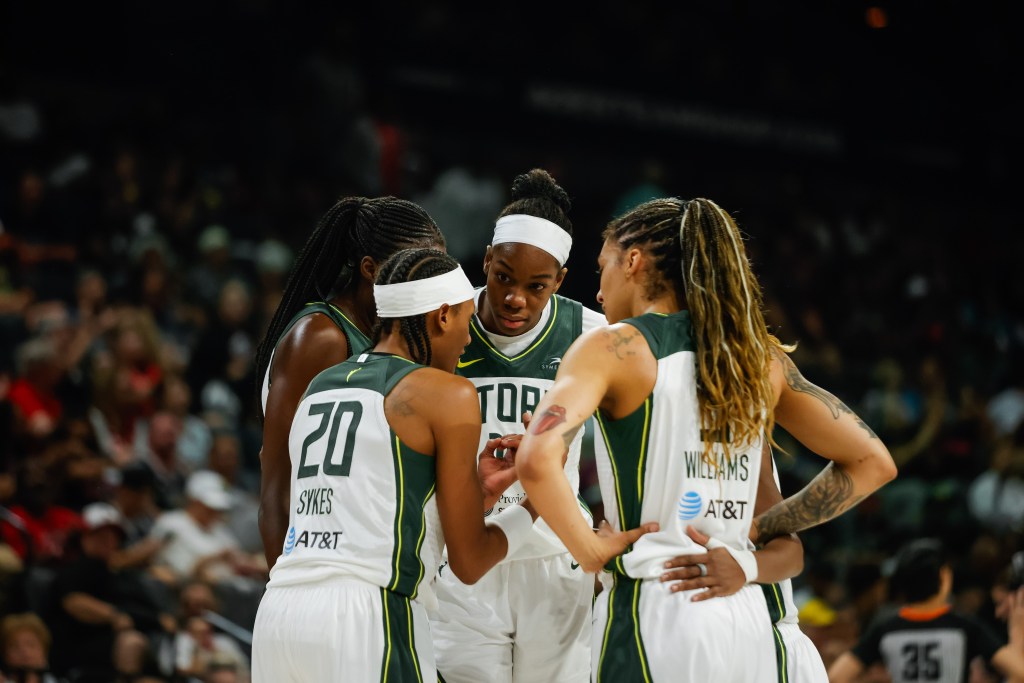 Brittney Sykes speaks intently to her teammates as Dominique Malonga and Gabby Williams clearly focus on what she is saying and gesturing with her hands.
