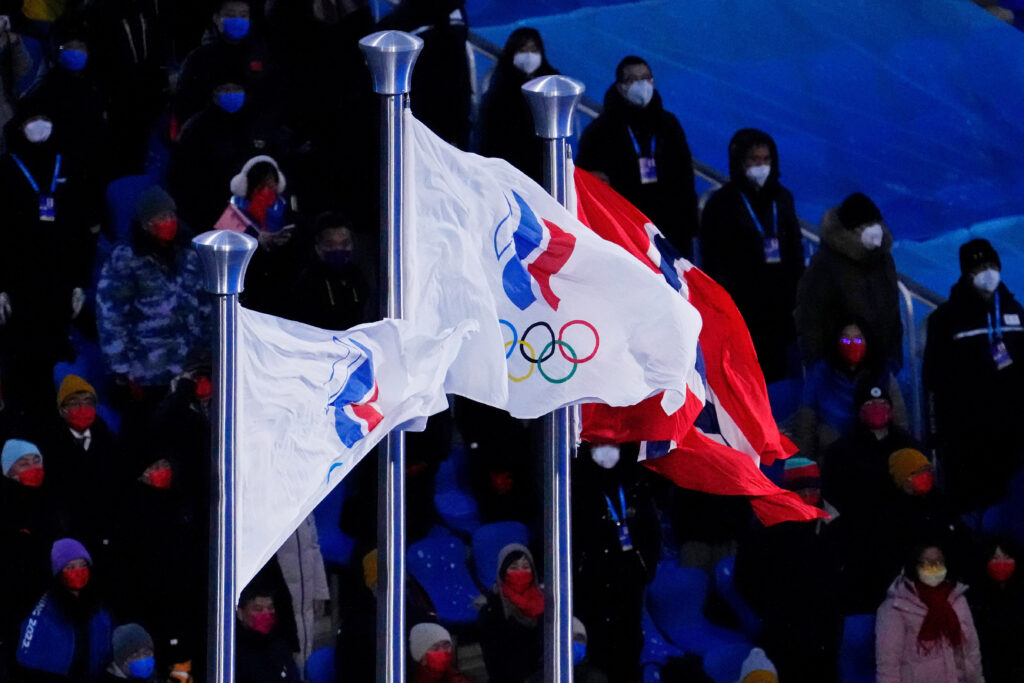 A white flag with a red and blue torch and the Olympic rings in red and blue beneath that.