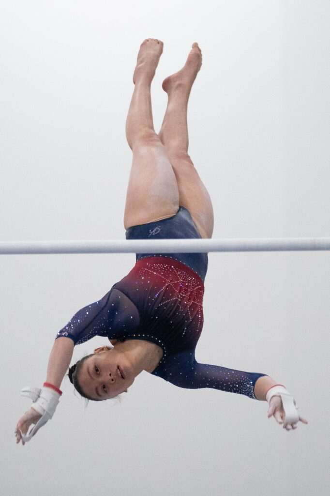A gymnast in a blue and red leotard competes on the unevent bars. 