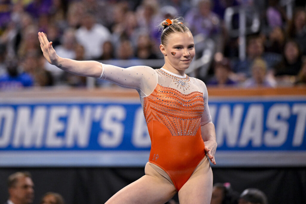 A gymnast in an orange and white leotard competes on the floor exercise.