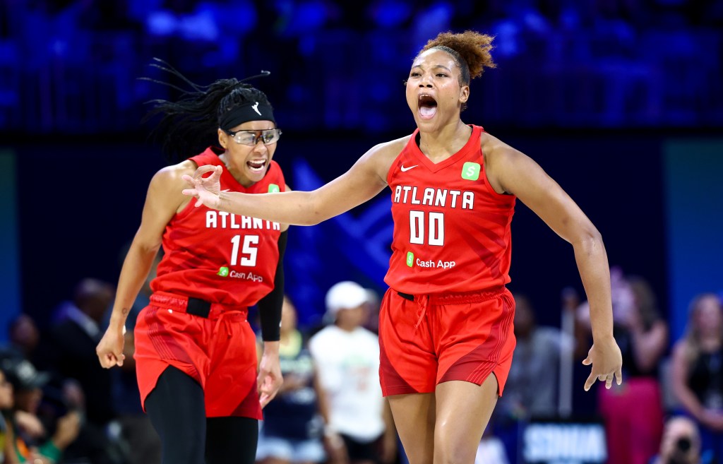 Two players in red Atlanta Dream jerseys cheer on the court in the middle of a game. 