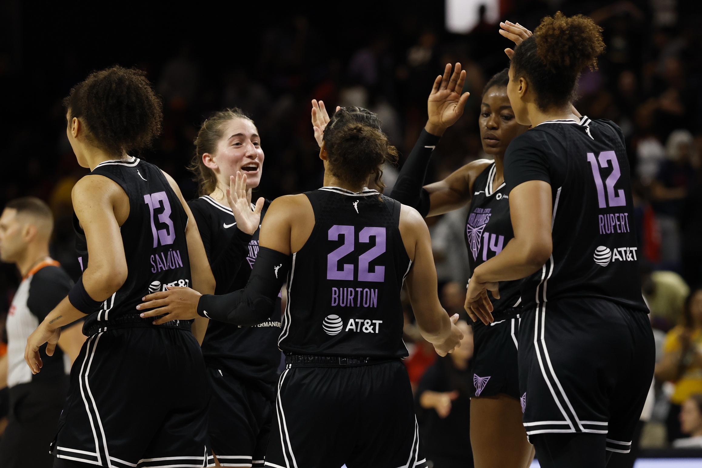 Golden State Valkyries players Veronica Burton, Kate Martin, Janelle Salaun, Temi Fagbenle and Iliana Rupert high-five each other after a game. They are standing roughly in a circle, wearing black uniforms with light purple numbers and white trim.