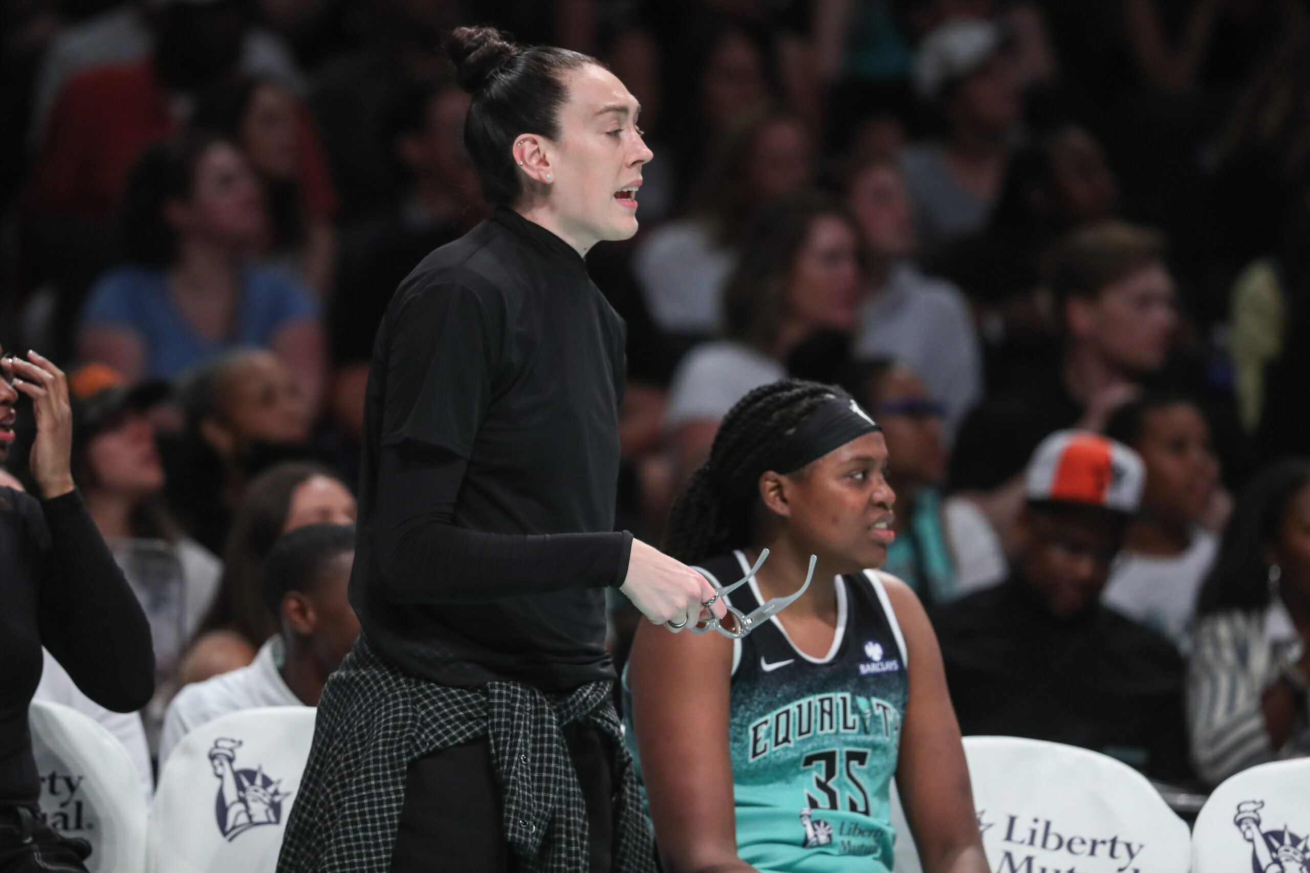 Breanna Stewart is next to Jonquel Jones while Stewart stands up and looks on from the bench during her month out.