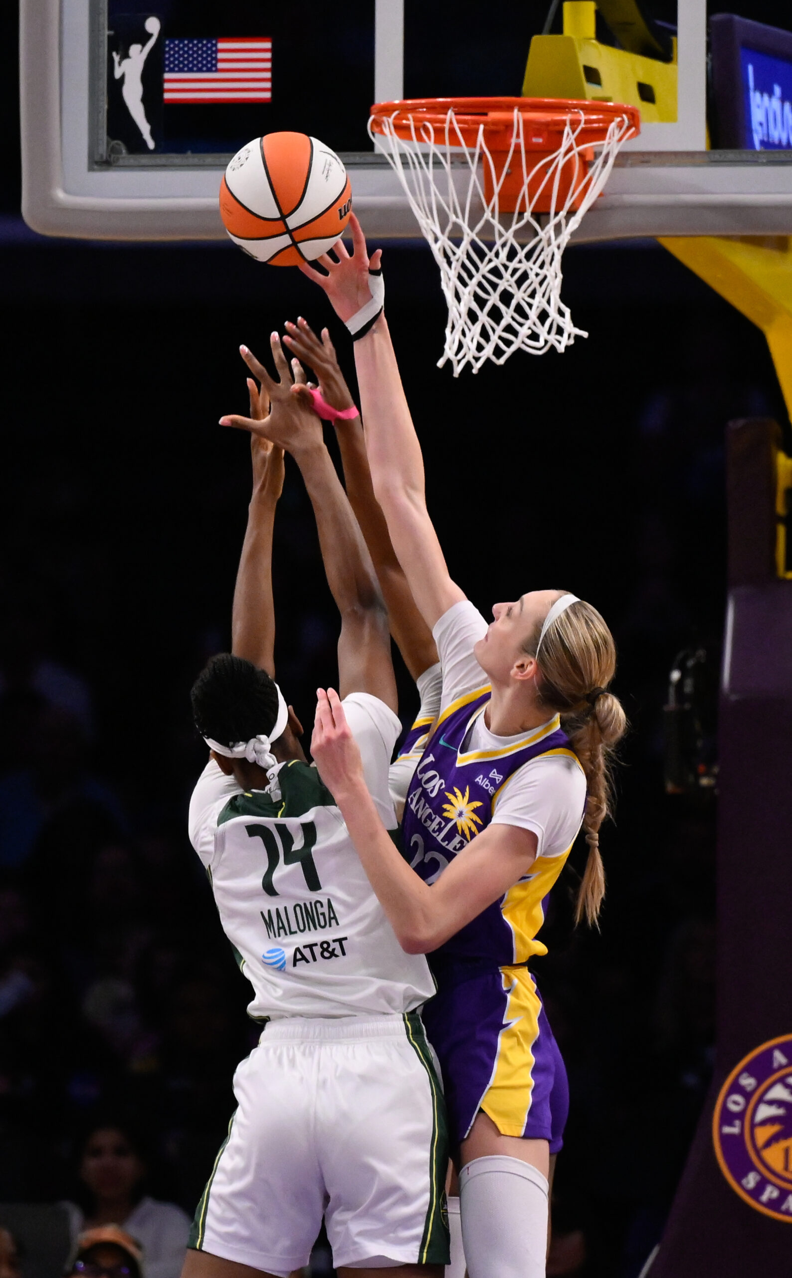 Two players wearing white uniforms battle for the ball on the court under a basket.
