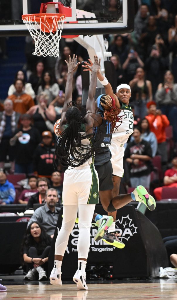 Rhyne Howard tries to score while sandwiched between Ezi Magbegor, whose arms are straight up in the air, and Brittney Sykes who is mid-air reach out to try and block the shot.