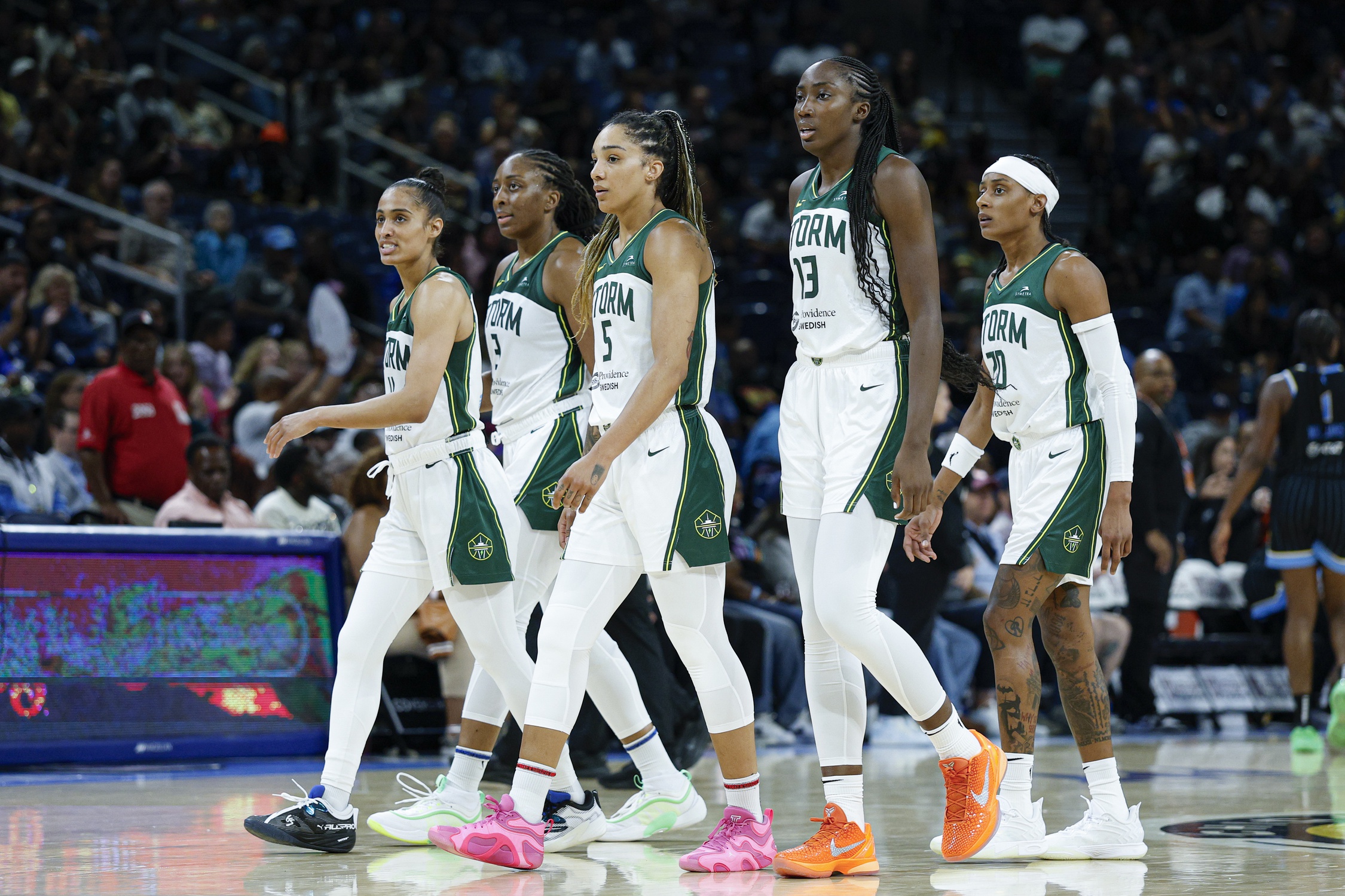 Five Seattle Storm players are shown in profile, walking back to their bench during a game.