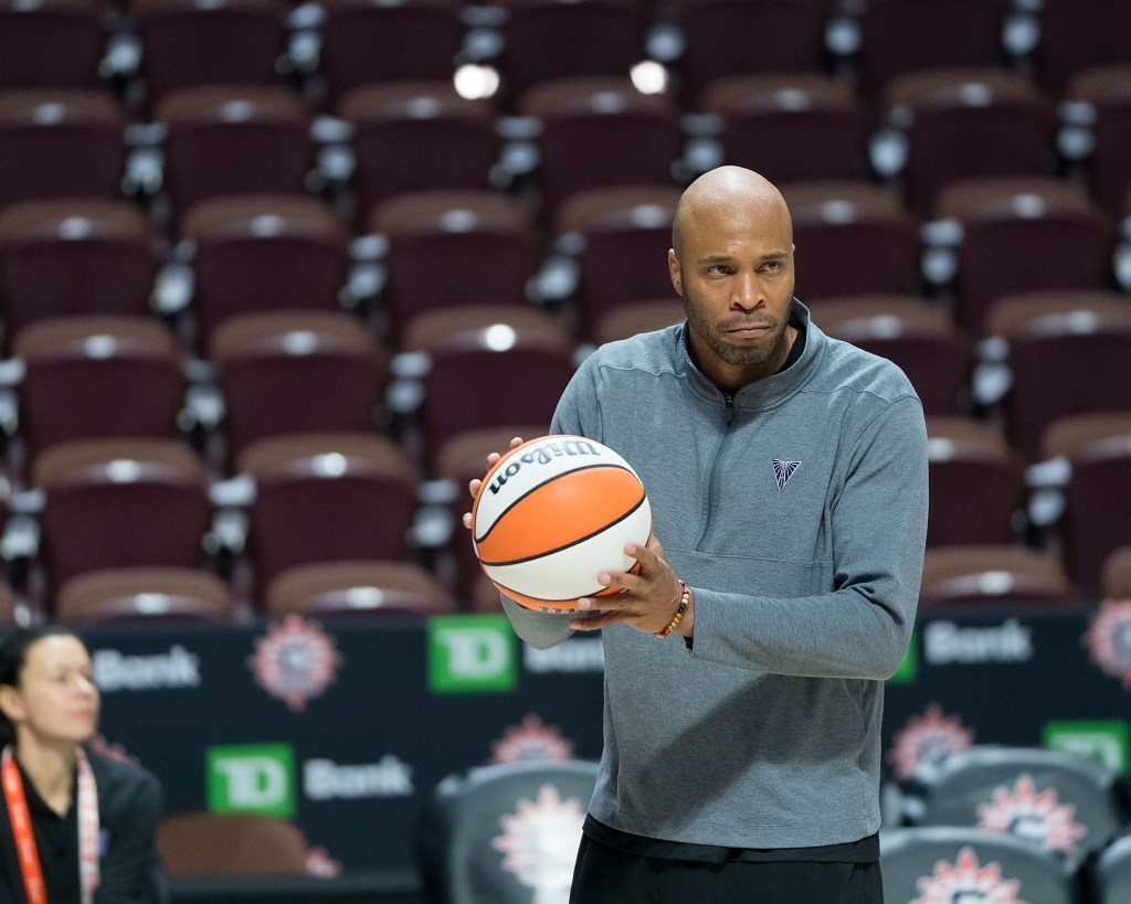 Golden State Valkyries assistant coach Kasib Powell holds a basketball with both hands during warmups. He is looking forward, and the empty stands are visible behind him.