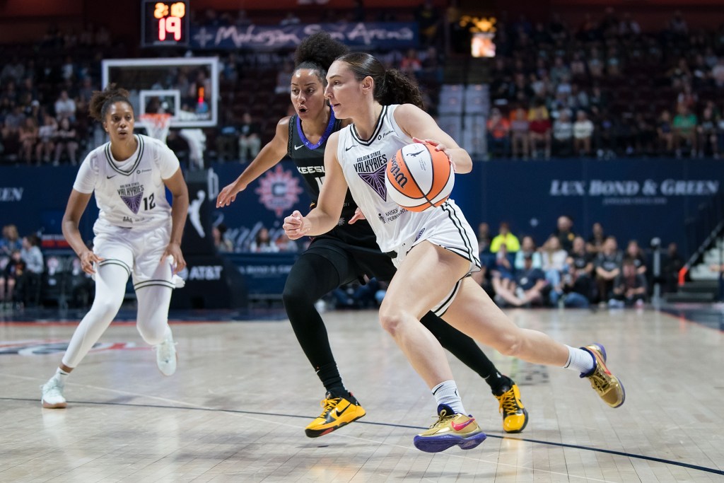 Golden State Valkyries guard Carla Leite drives to the basket as Connecticut Sun guard Bria Hartley defends her. They are shown from the front as Valkyries forward Iliana Rupert and a large crowd are shown in the backgroud.