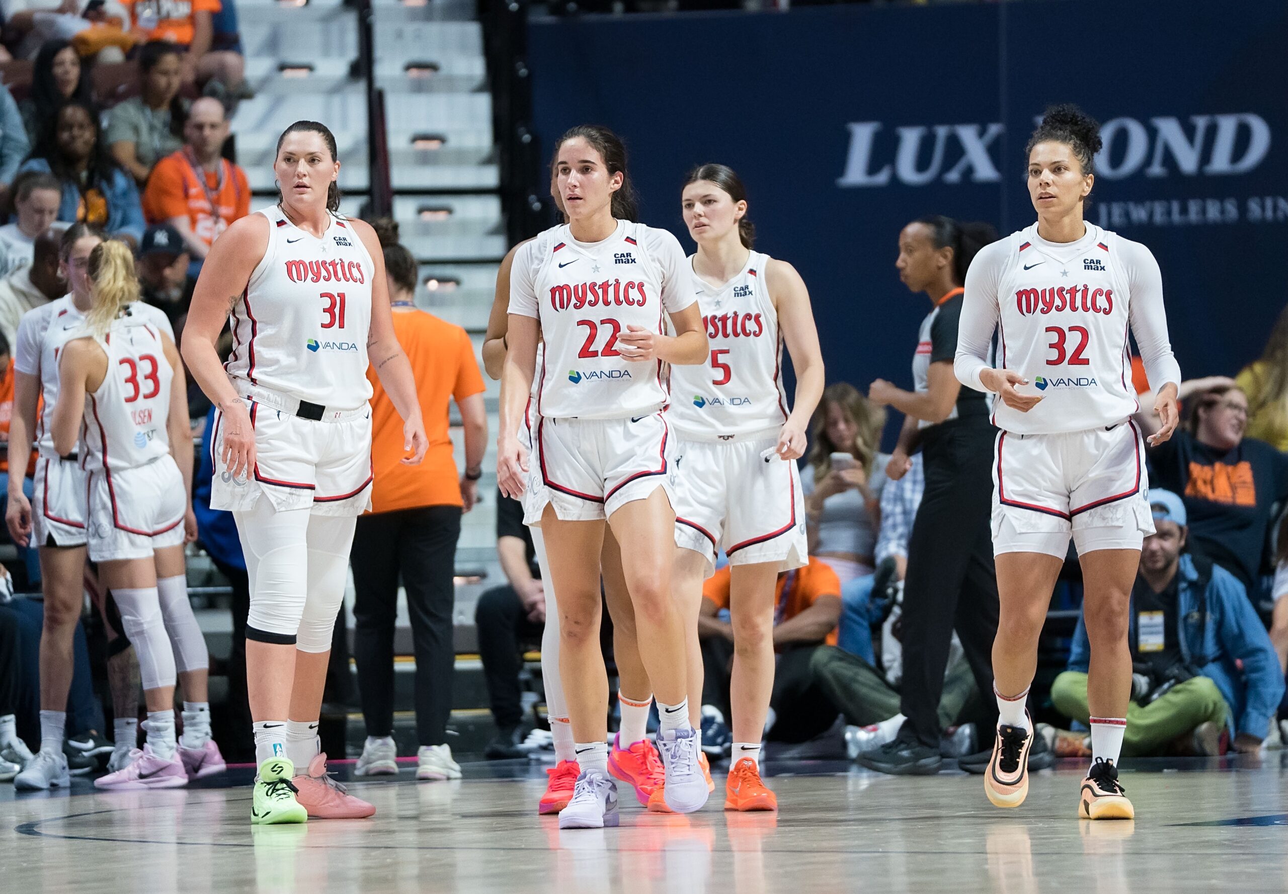 Washington Mystics players stand on the court and look forward at something off camera, as if they are waiting for something.