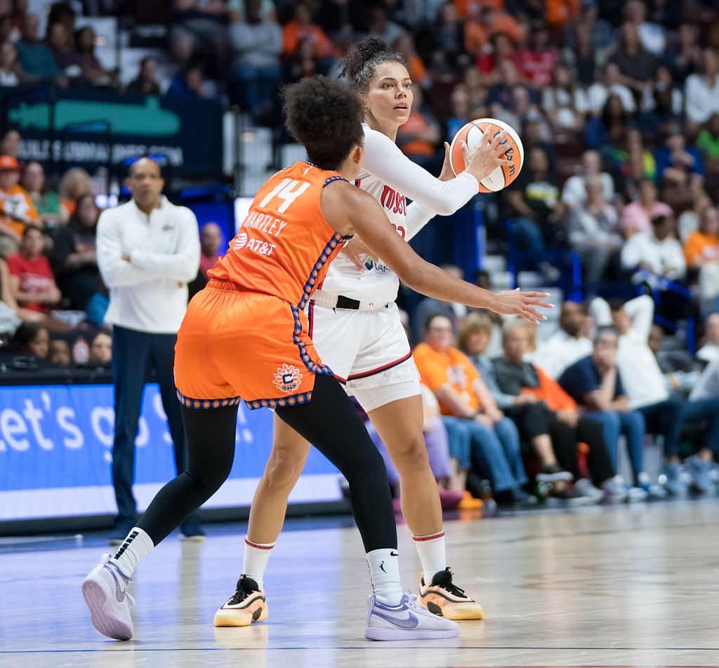 Washington Mystics forward Alysha Clark holds the ball with both hands near her left shoulder. She has her eyes up, looking for a pass as Connecticut Sun guard Bria Hartley defends her tightly.