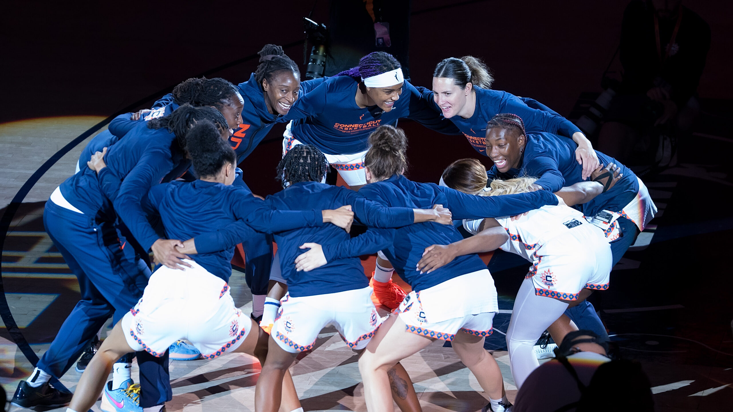 The Connecticut Sun moving in a circular motion back and forth in a huddle while smiling before a game.