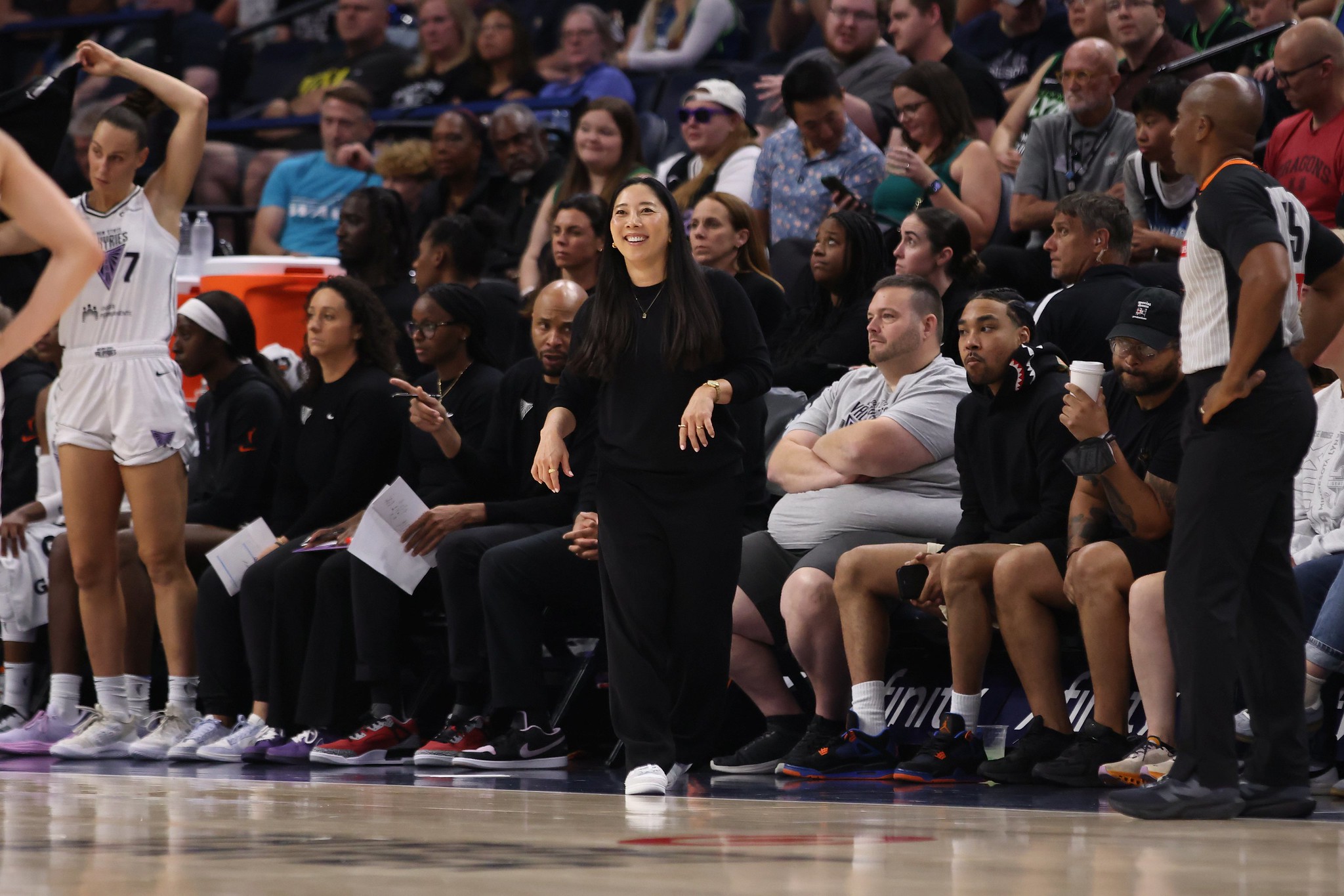 Golden State Valkyries head coach Natalie Nakase smiles as she coaches her team. She is shown from the front with a large crowd behind her.