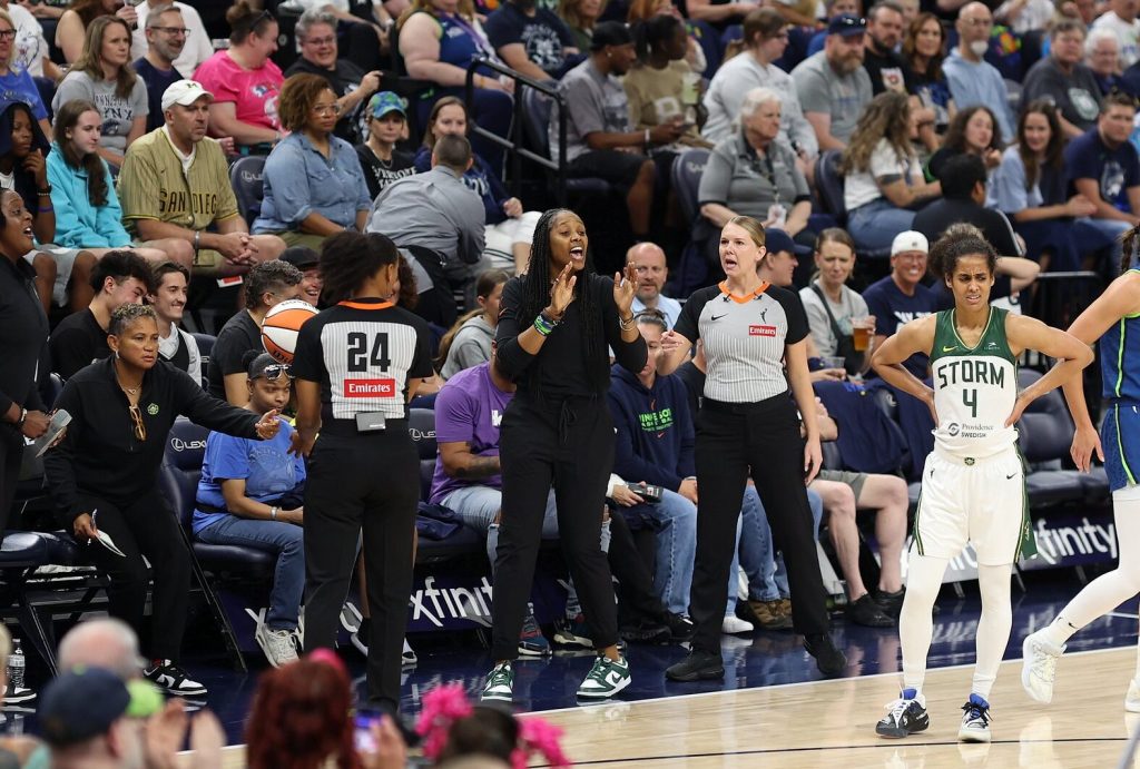 Then-Seattle Storm head coach Noelle Quinn motions with her hands and yells something toward the court. The referees on either side of her exchange words, and Storm point guard Skylar Diggins looks frustrated on the court.