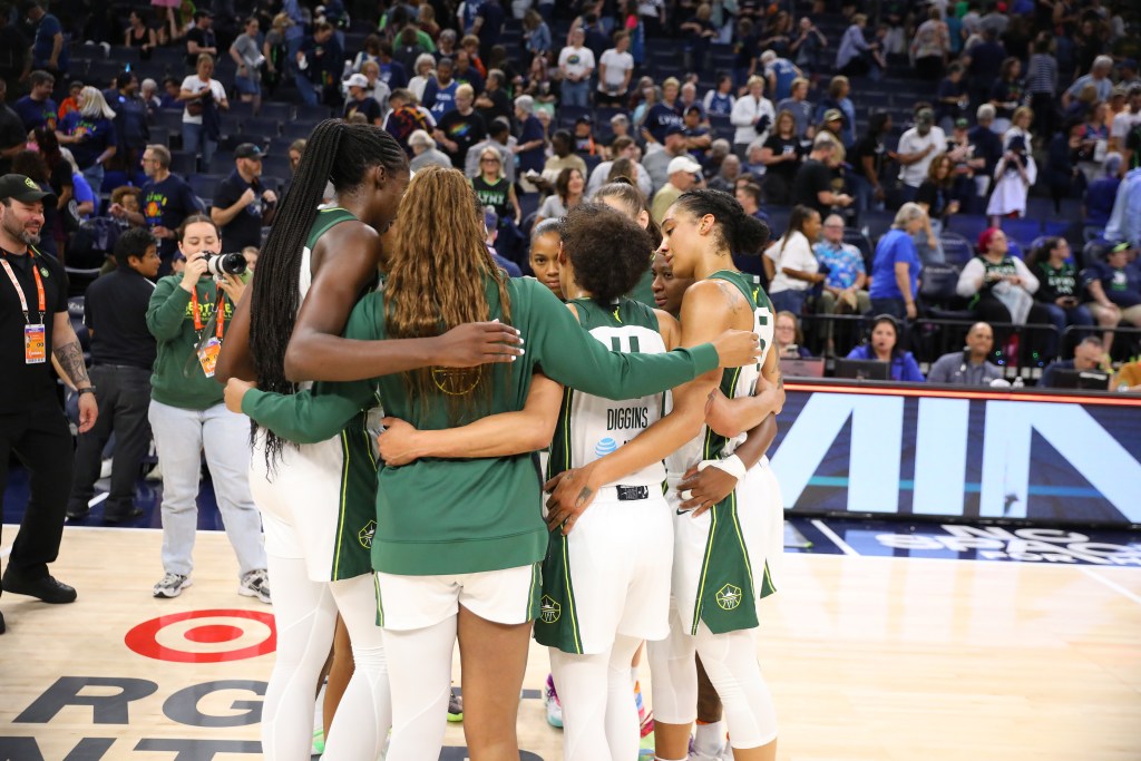 Seattle Storm players gather near the Target Center logo after a game in Minnesota. They put their arms around each other as they talk.