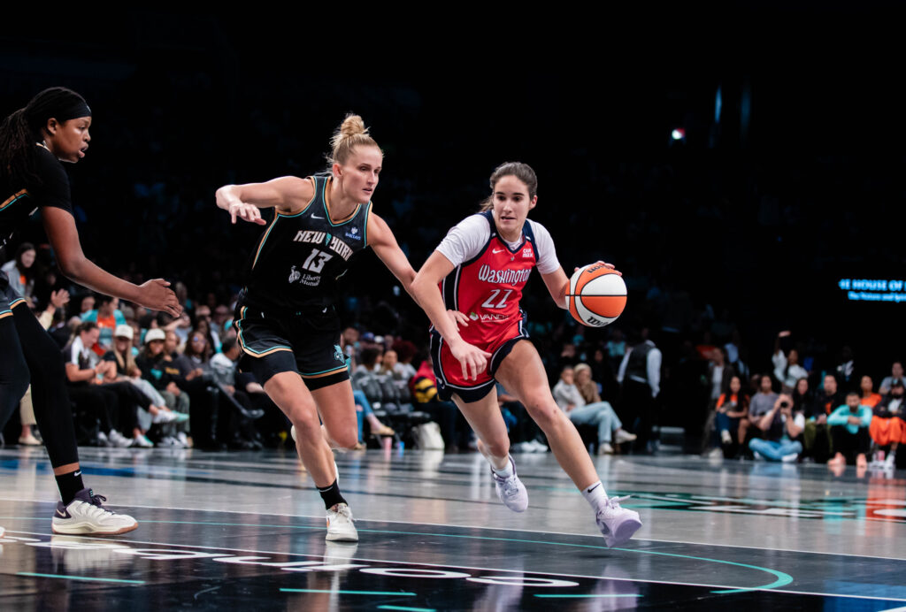 Photo of Washington's Sonia Citron driving toward the lane. New York's Leonie Fiebich is between her and the basket.