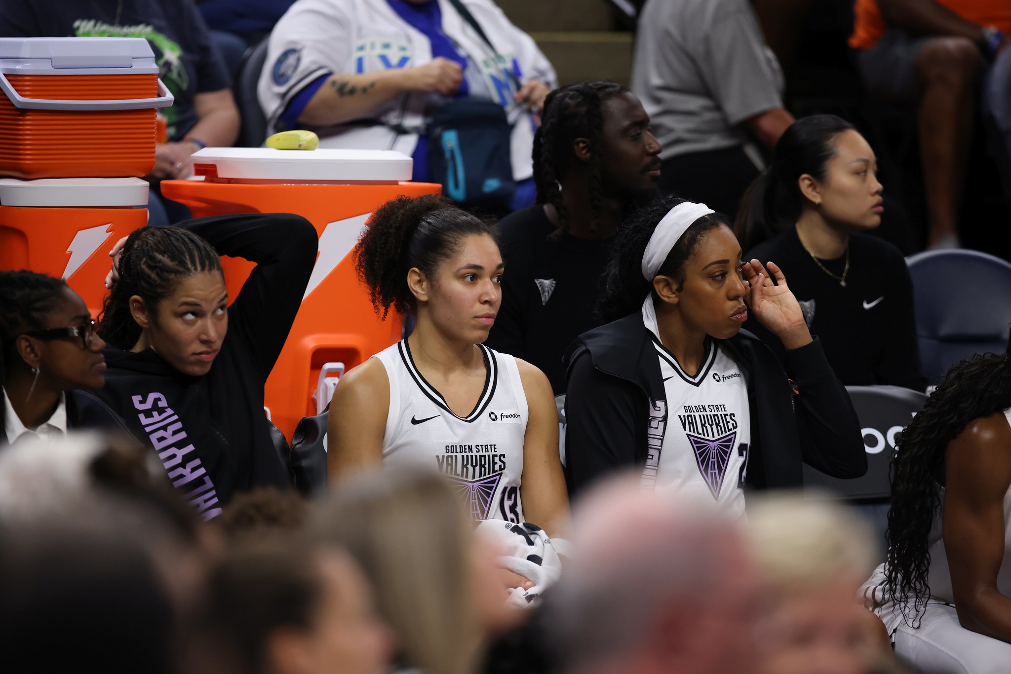 Valkyries guard Veronica Burton and forwards Janelle Salaun and Monique Billings sit on the bench. They are shown from the front with people in the backgroud.