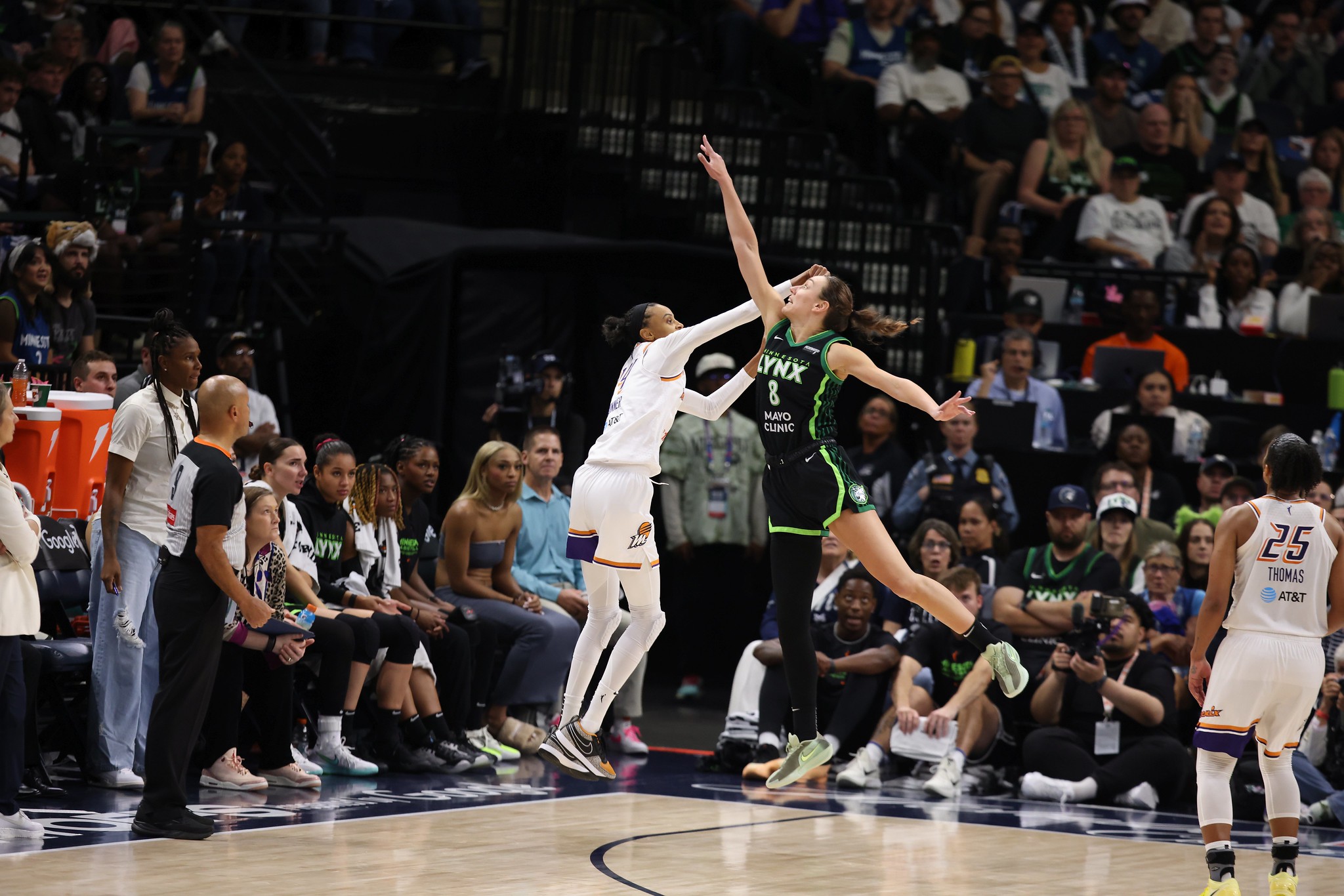 A player in a green jersey jumps over a player in a white jersey on a basketball court