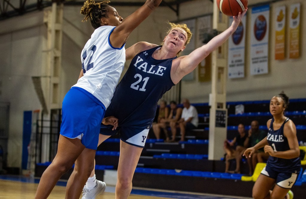Yale guard Kiley Capstraw leans to her left and extends her left arm fully as she tries to shoot around an Antibes Select defender.