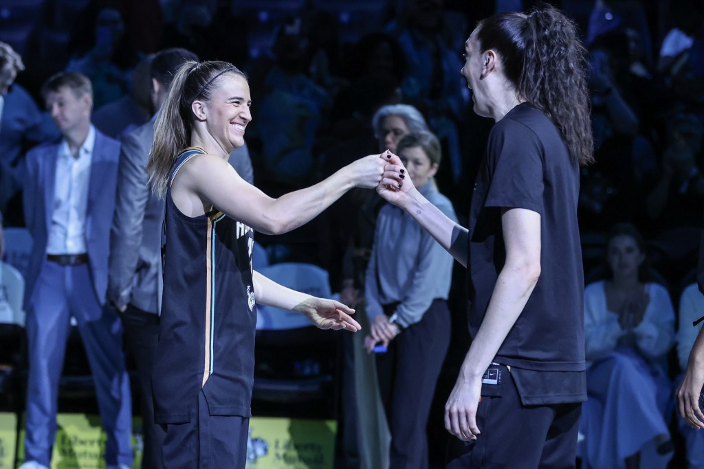 New York Liberty guard Sabrina Ionescu and forward Breanna Stewart are each shown from the side as they press their right hands together in a handshake.