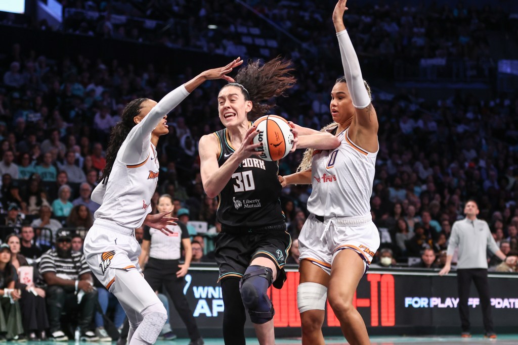 Wearing a black brace on her left knee, New York Liberty forward Breanna Stewart holds the ball with both hands in front of her body. She looks to split Phoenix Mercury forwards DeWanna Bonner and Satou Sabally.