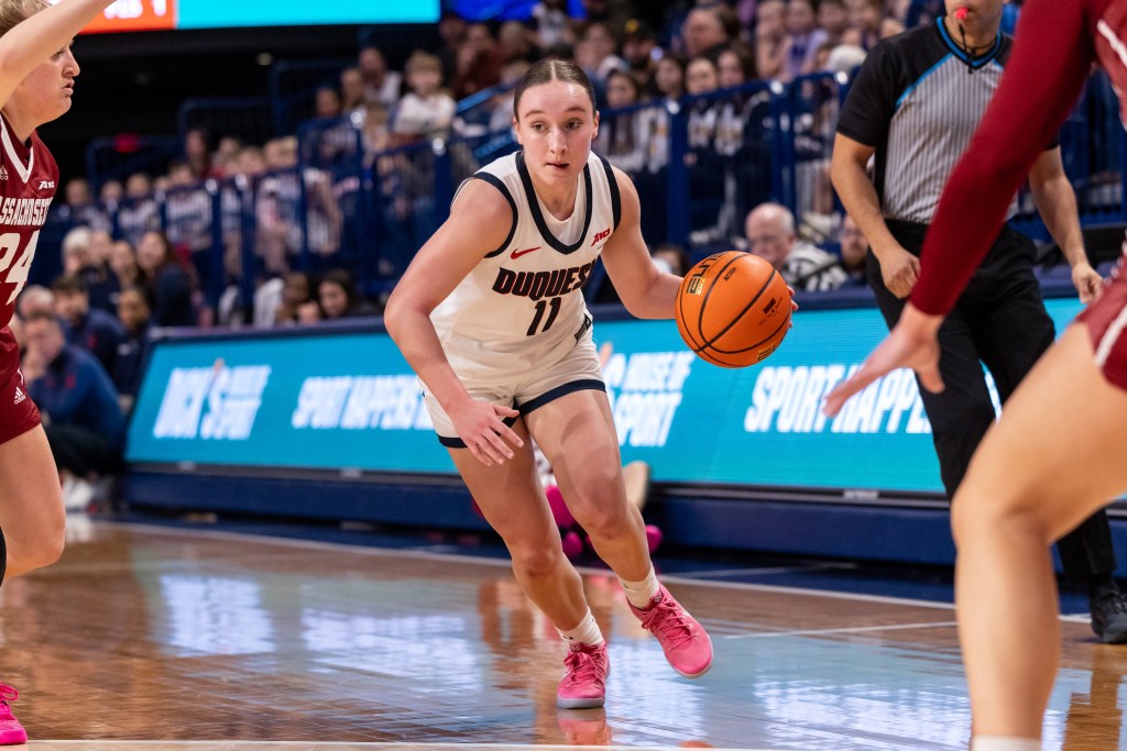 Duquesne guard Mackenzie Blackford dribbles the ball with her left hand, looking to split two UMass defenders.