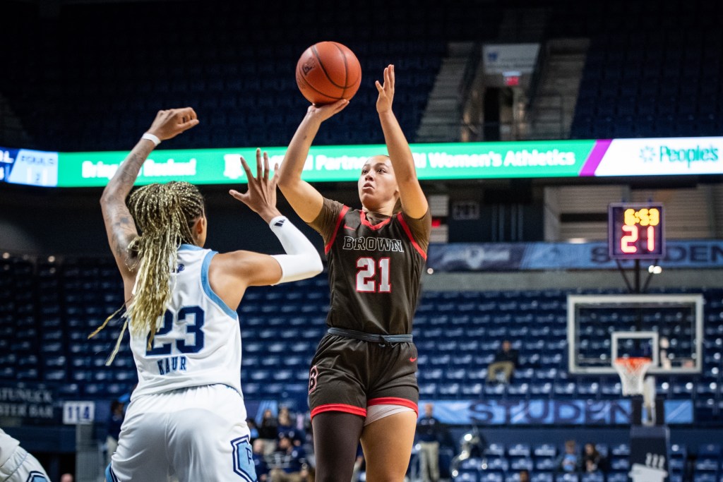 Brown guard Grace Arnolie shoots a right-handed jump shot over a Rhode Island defender. In the background, the shot clock shows 21 seconds left.