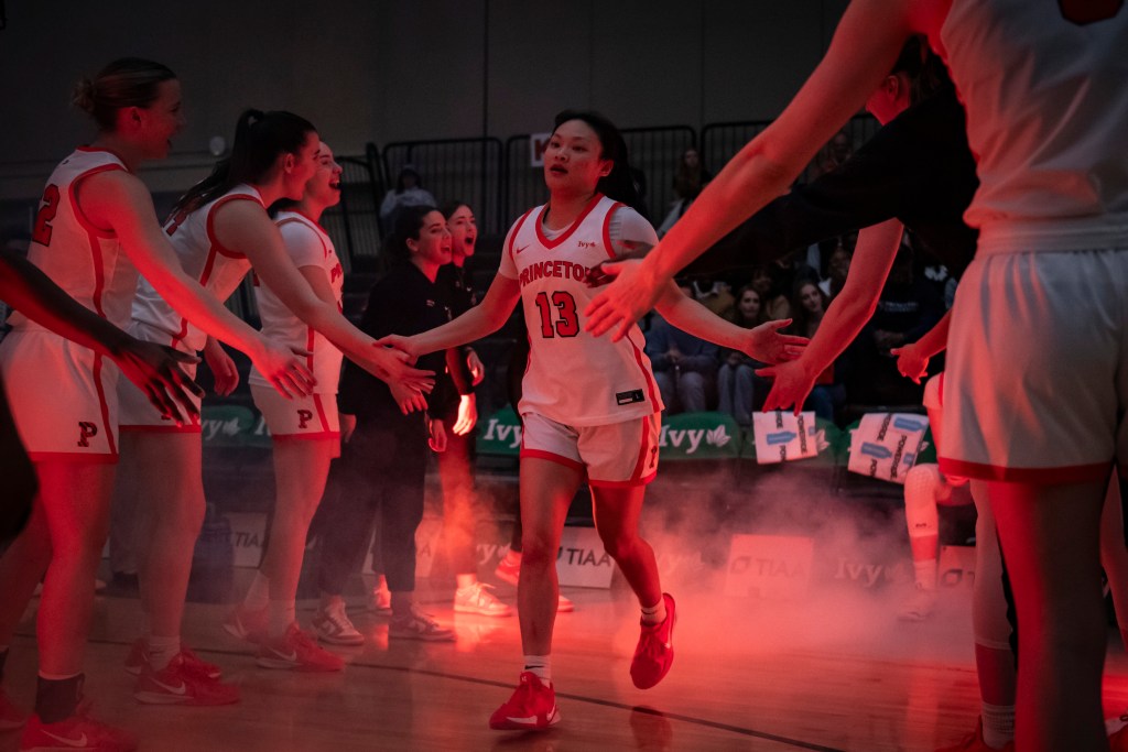 Princeton guard Ashley Chea runs on the court and high-fives her teammates as she’s introduced as a starter. The arena is dark and there is a reddish glow from the lighting and special effects.