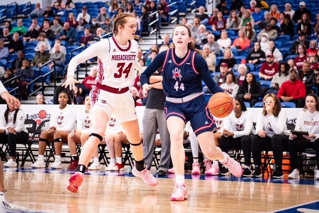 Richmond forward Maggie Doogan dribbles the ball with her left hand near the baseline. A UMass forward guards her tightly, cutting off her angle to get higher up the court.