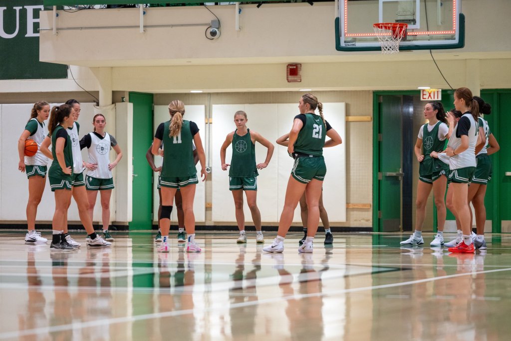 Dartmouth players, wearing green and white practice jerseys, stand in a large circle during a preseason practice.