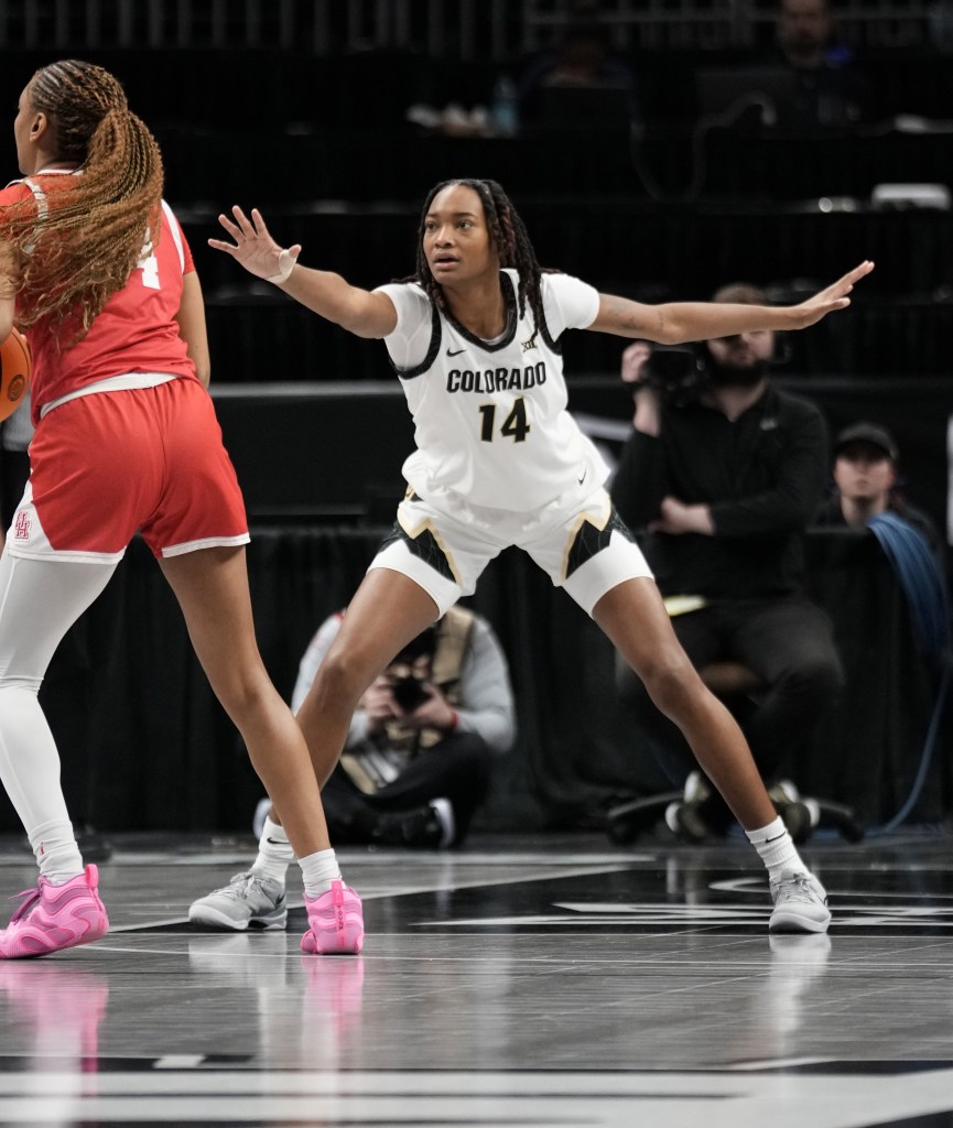 Colorado forward Jade Masogayo sits in a defensive stance near the free-throw line. Her right arm is extended toward her matchup, and her eyes are locked on the ball.