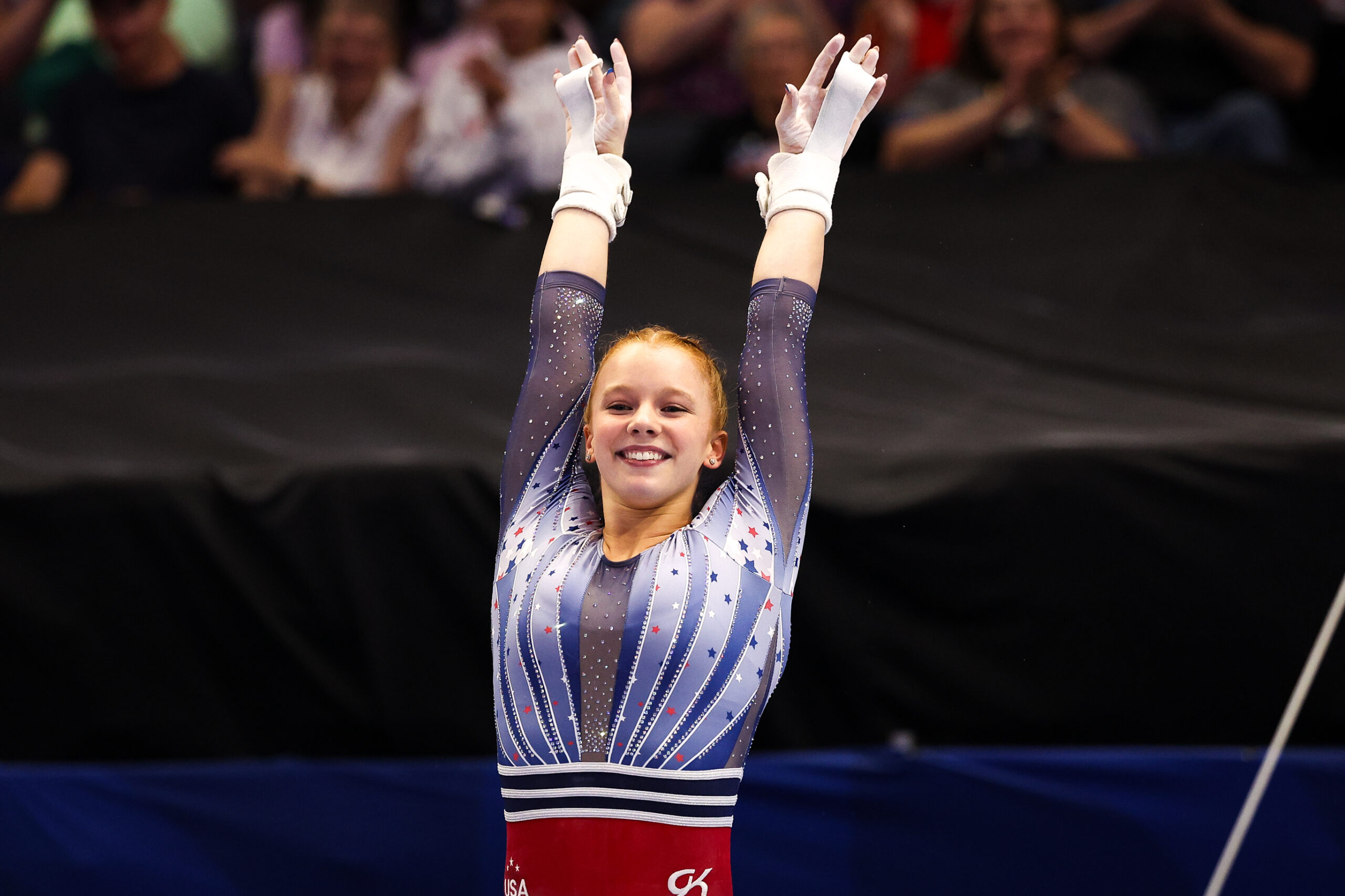 A gymnast in a red, white, and blue leotard celebrates a routine.